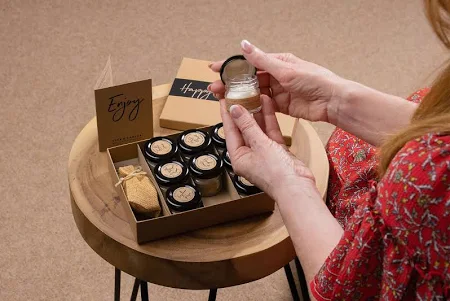 Hands opening beeswax candle jar on wooden table