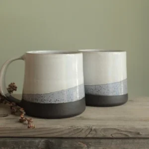Two minimalist porcelain mugs with layered glaze on wooden table